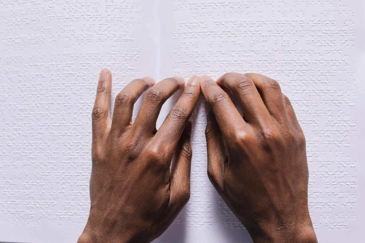 services-03 Close-up of hands reading a Braille book on a white background, illustrating tactile reading skills.
